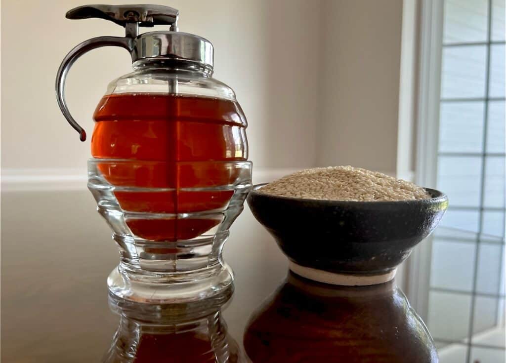 antique honey dispenser filled with honey and a hand made pottery bowl filled with sesame seeds.