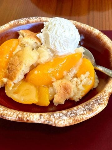 Bowl of peach cobbler with ice cream.