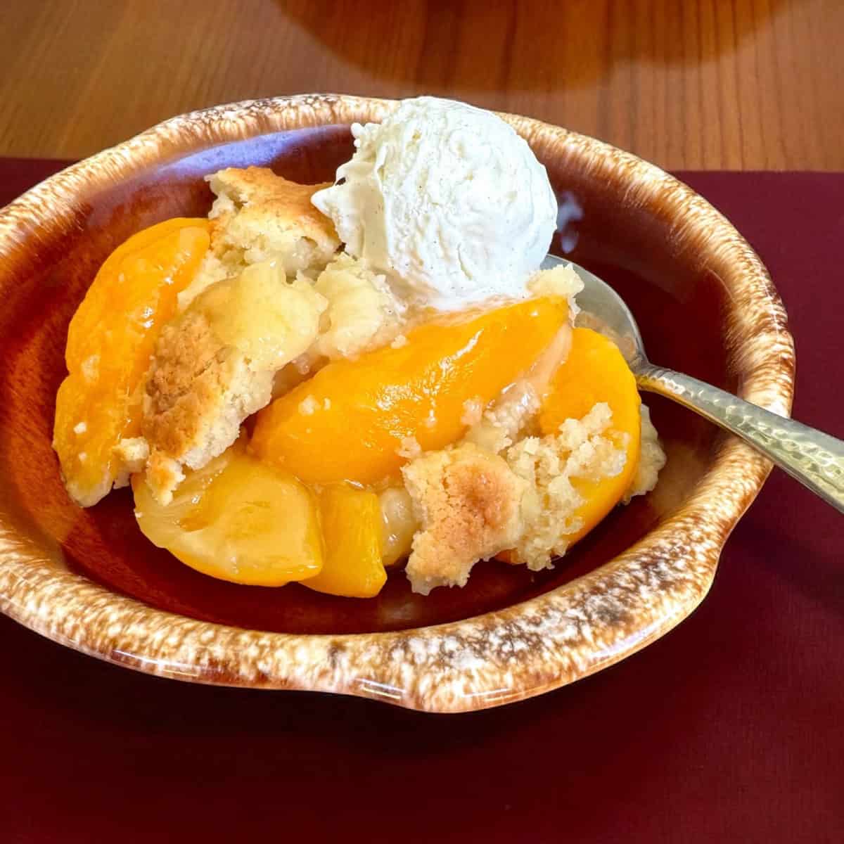 Bowl of peach cobbler with ice cream.