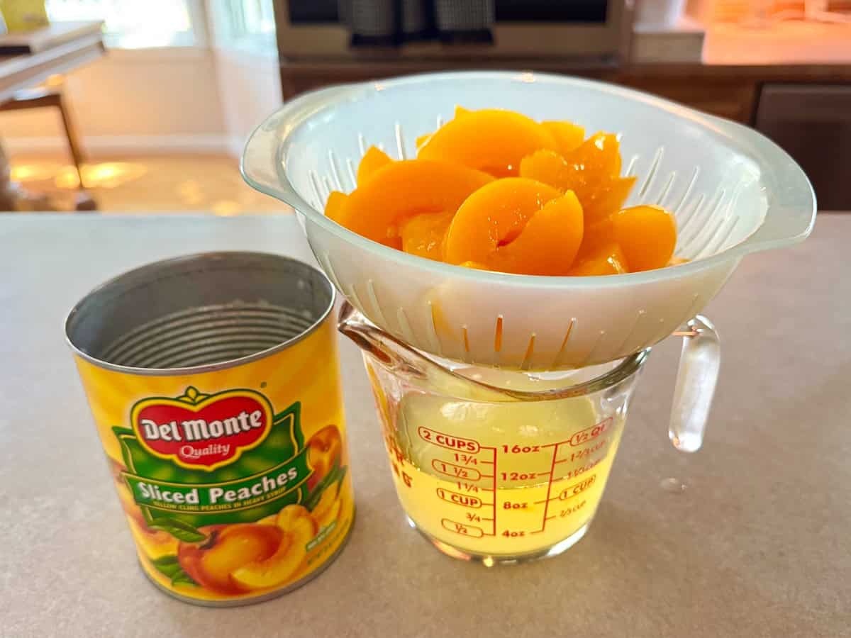 Straining canned peaches over a measuring cup.