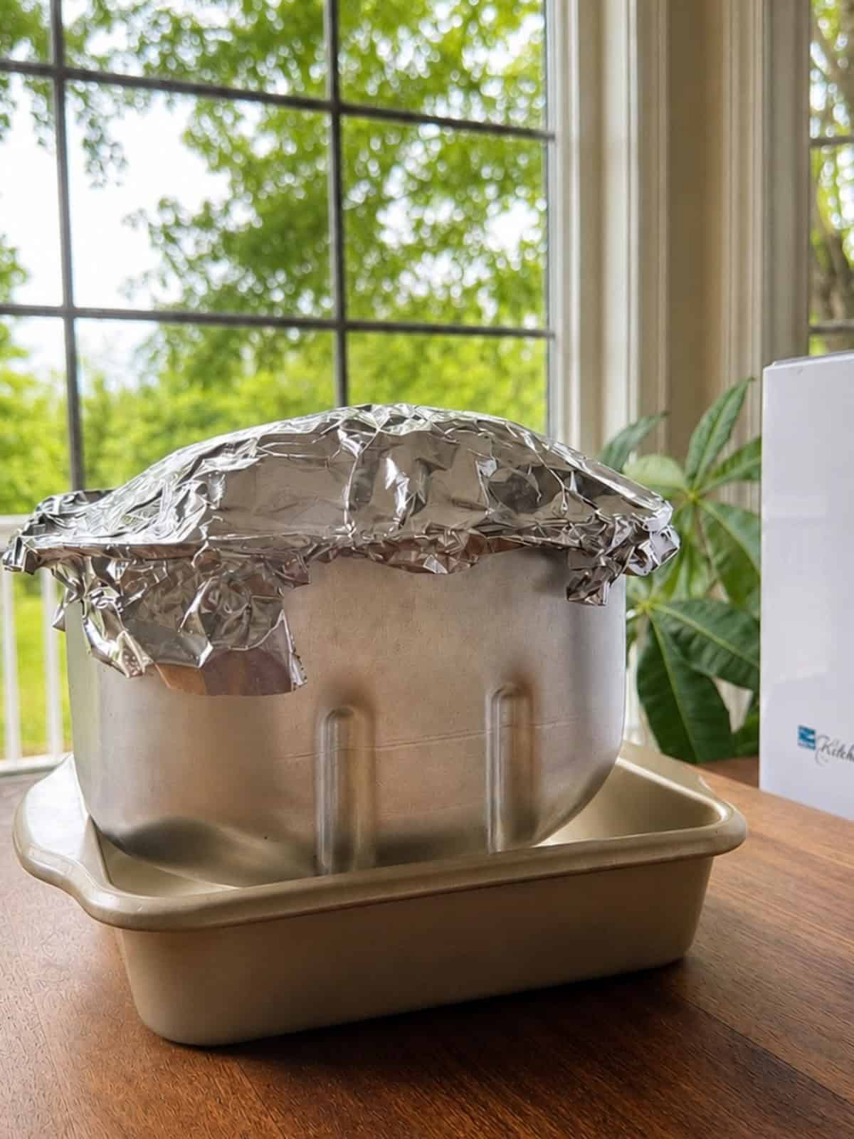 Bread machine pan with foil on top to seal in moisture of the bread.