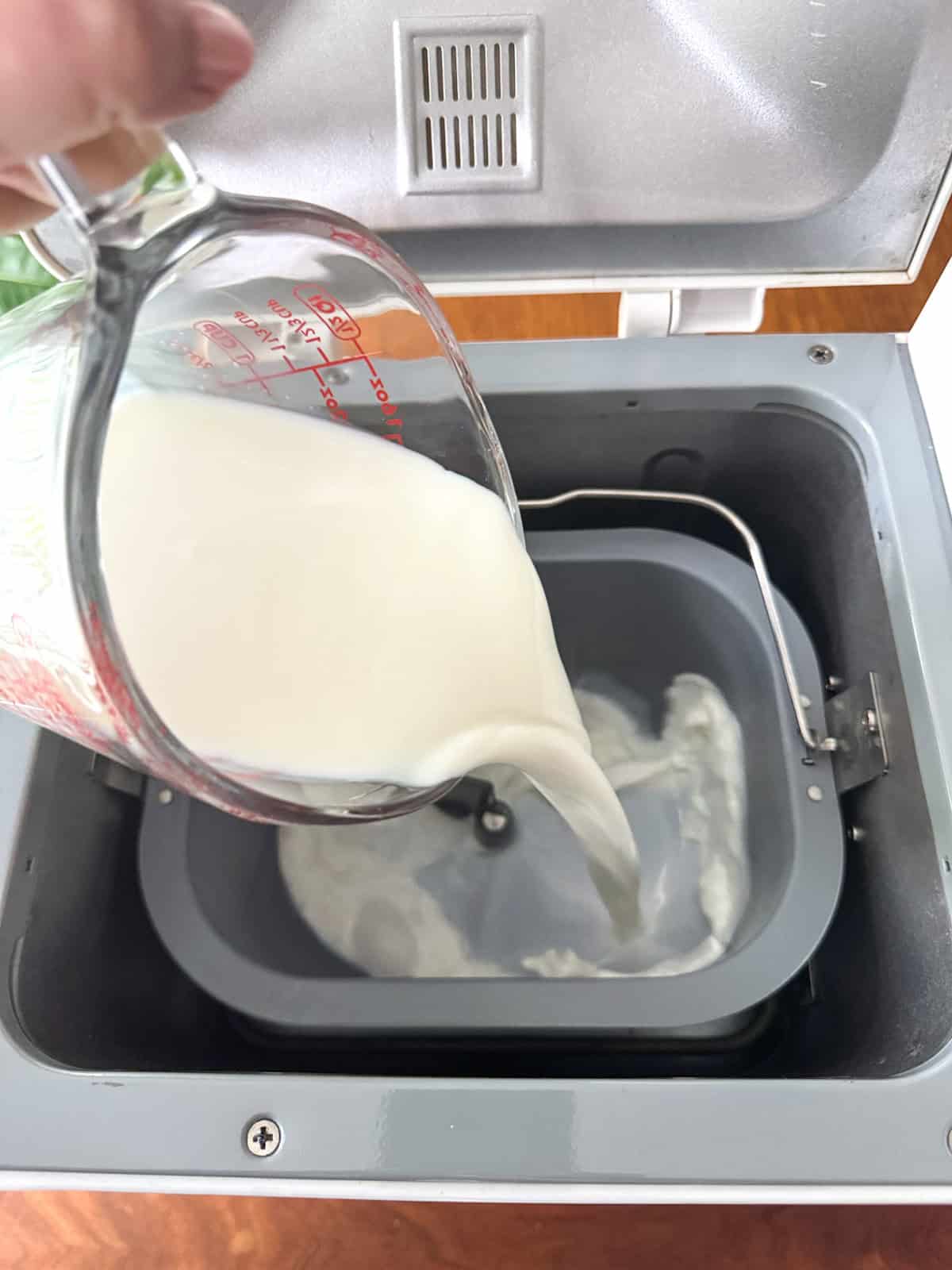 Adding milk to bread machine pan.